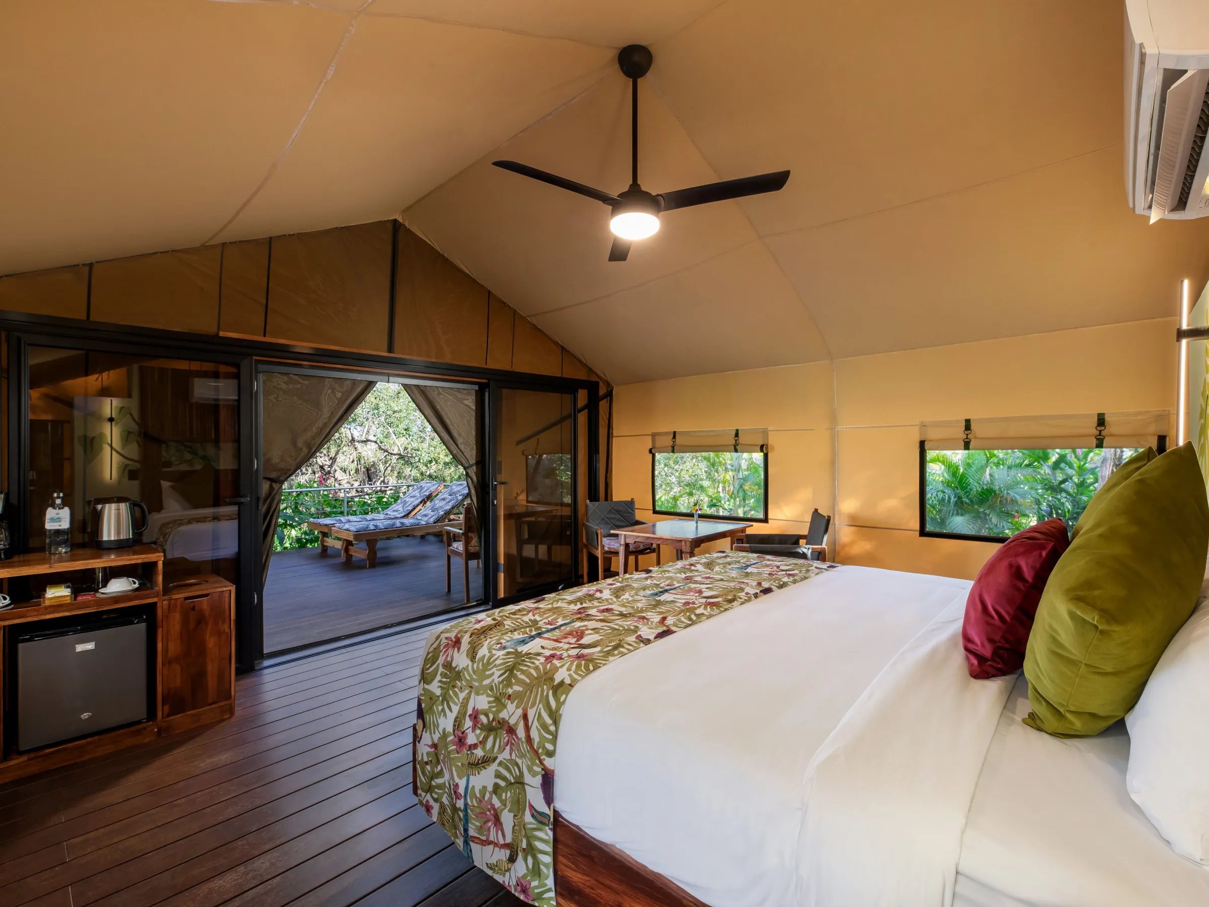 Glamping tent interior with bed, ceiling fan, sliding glass doors, and outdoor deck view.
