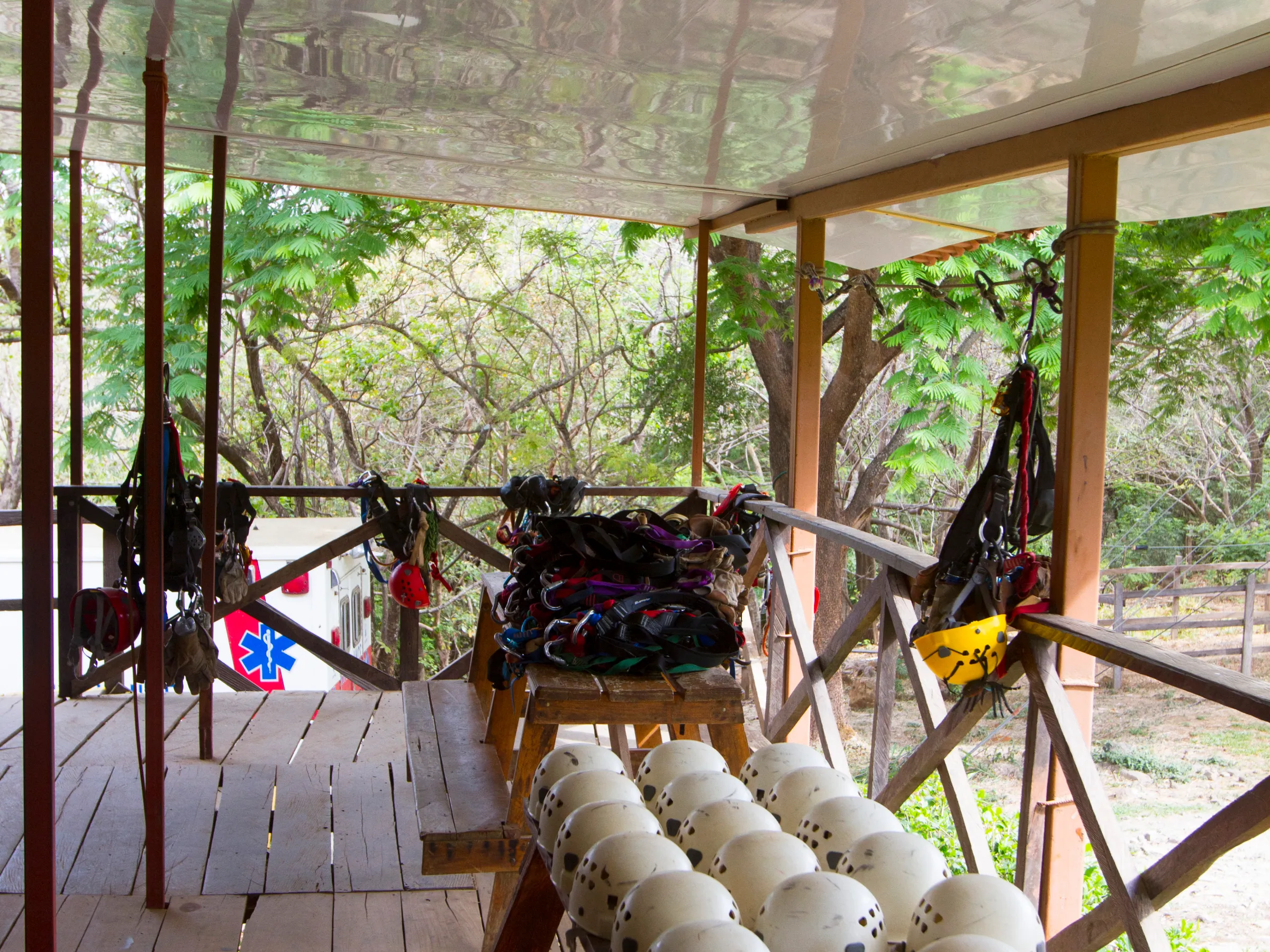 Wooden platform with helmets and harnesses near trees under a covered area.