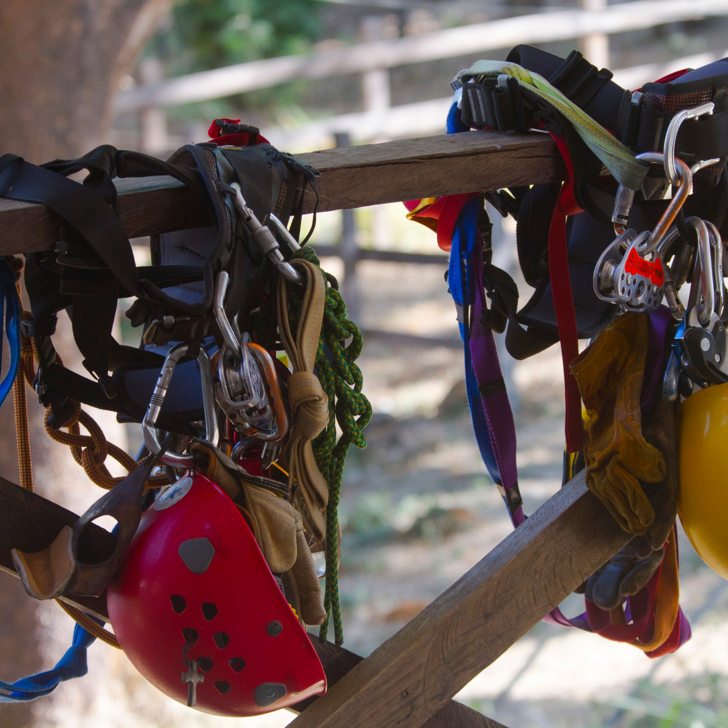Climbing gear including helmets and harnesses hanging on wooden fence.