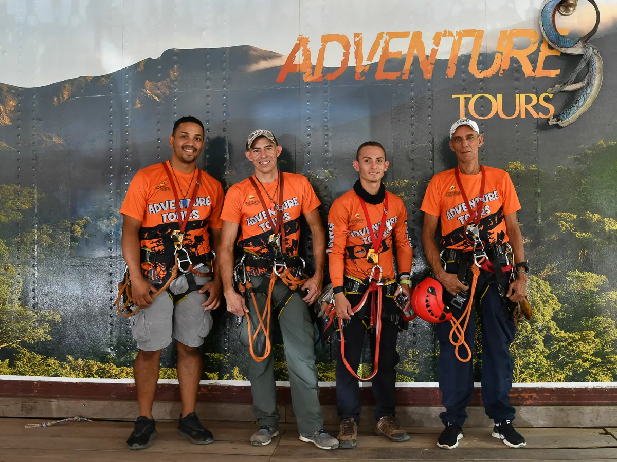 Four men in orange adventure gear posing in front of an 'Adventure Tours' sign.