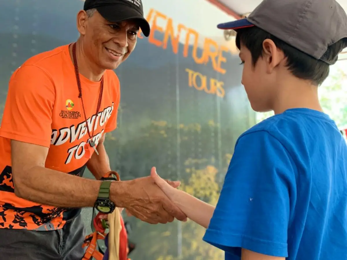 Man in orange shirt shakes hands with a boy in a blue shirt and cap.