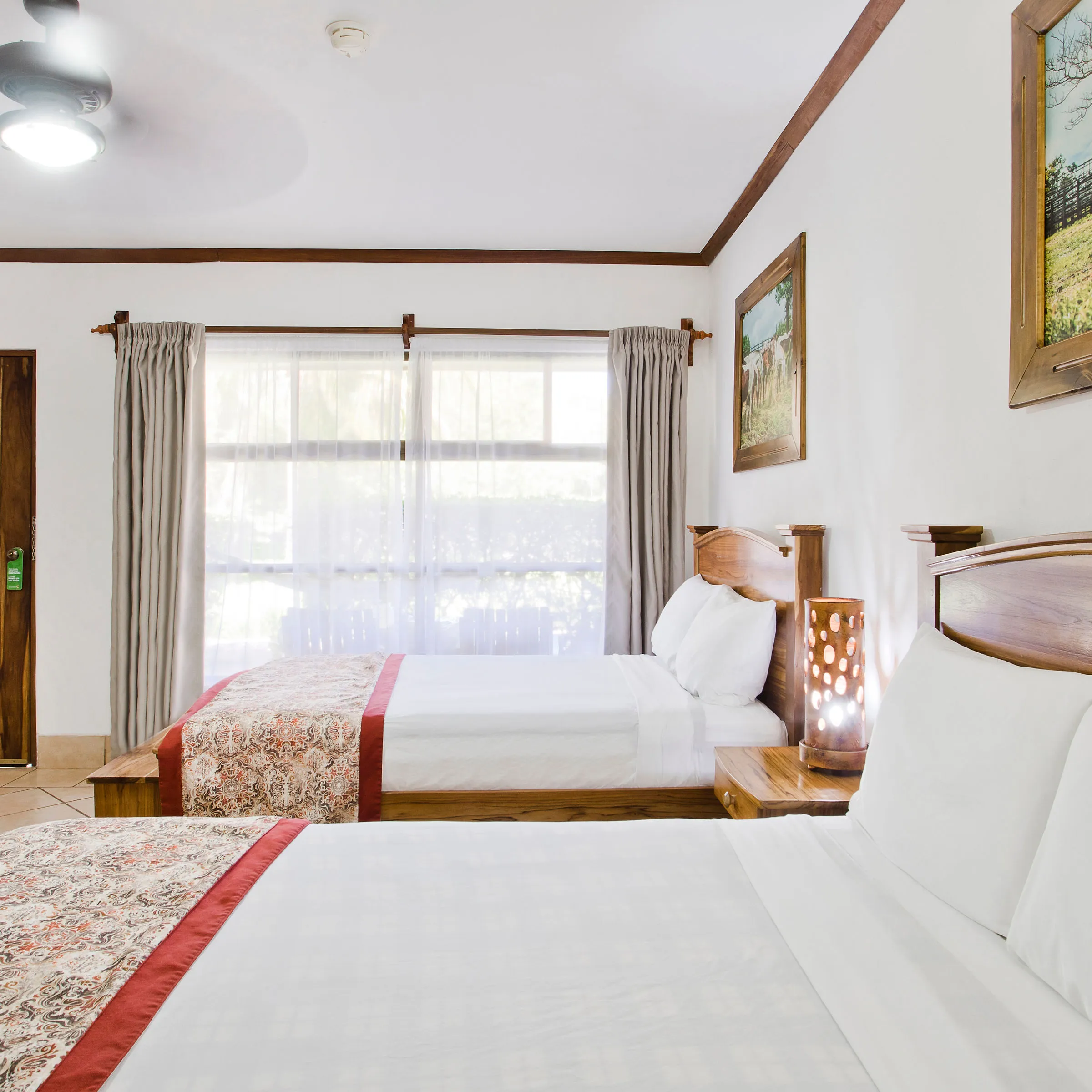 Bright hotel room with two beds, wooden headboards, and nature-themed decor.