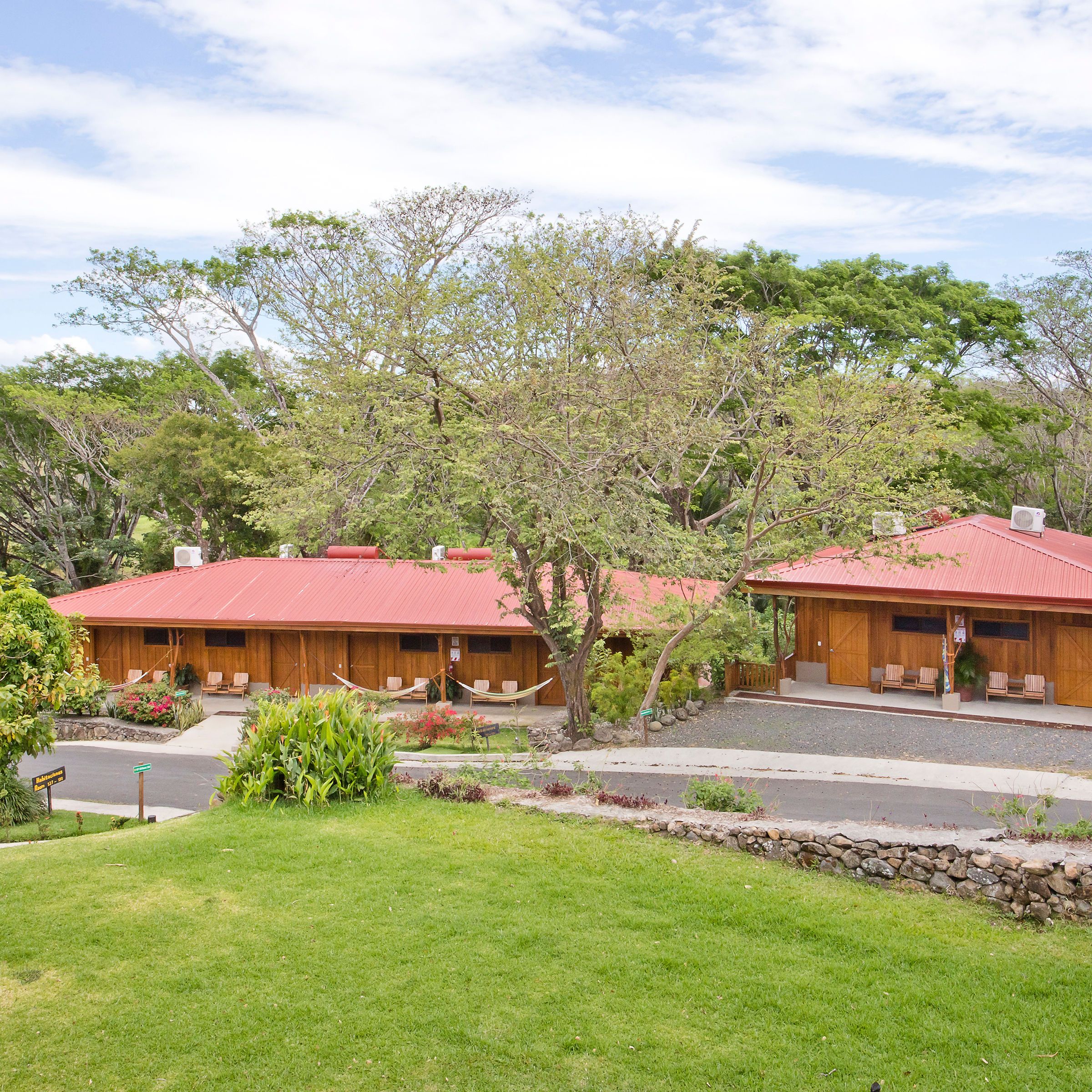 Red-roofed wooden buildings surrounded by trees and grass under a partly cloudy sky.