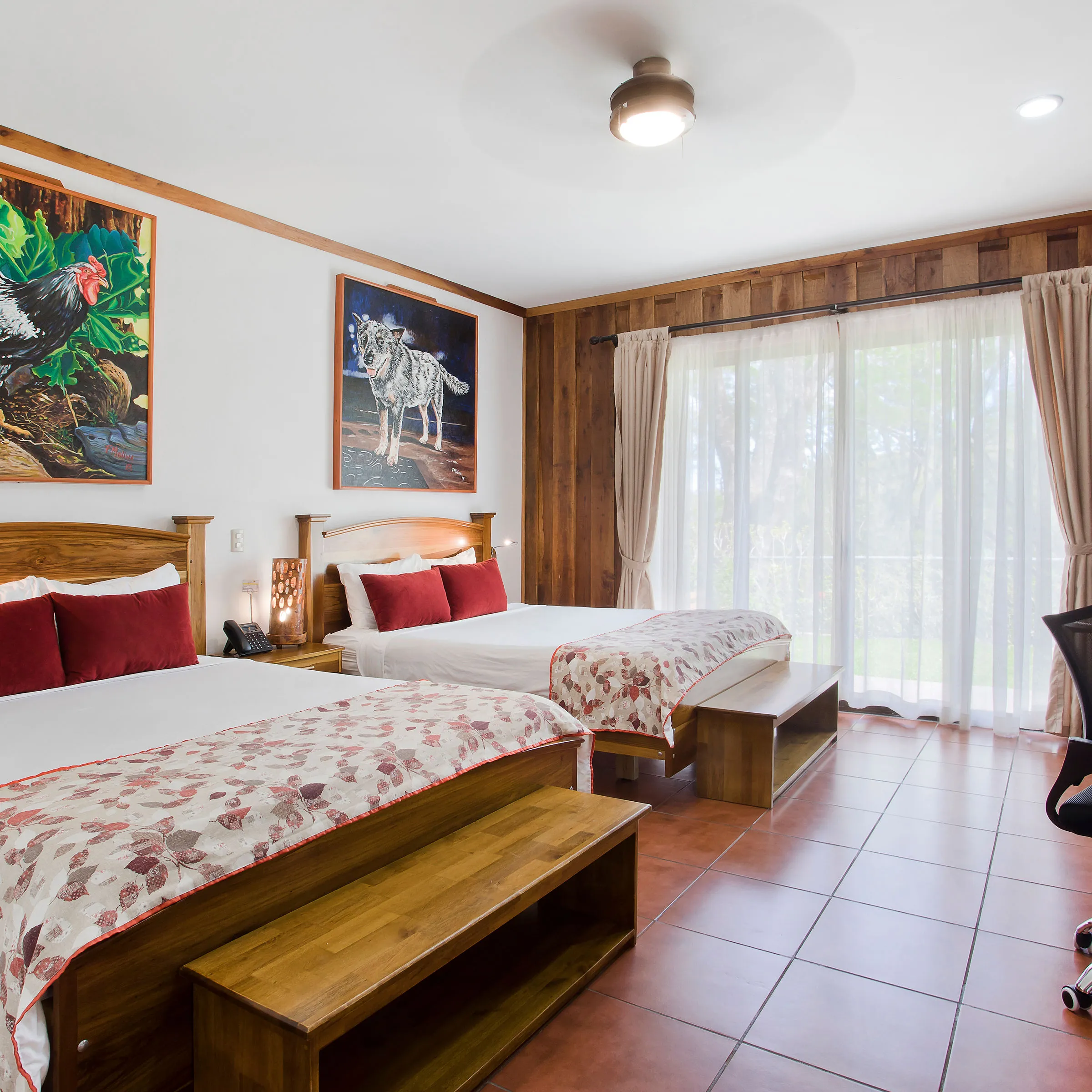 Wood-paneled room with two beds, art, desk, and large window with curtains.