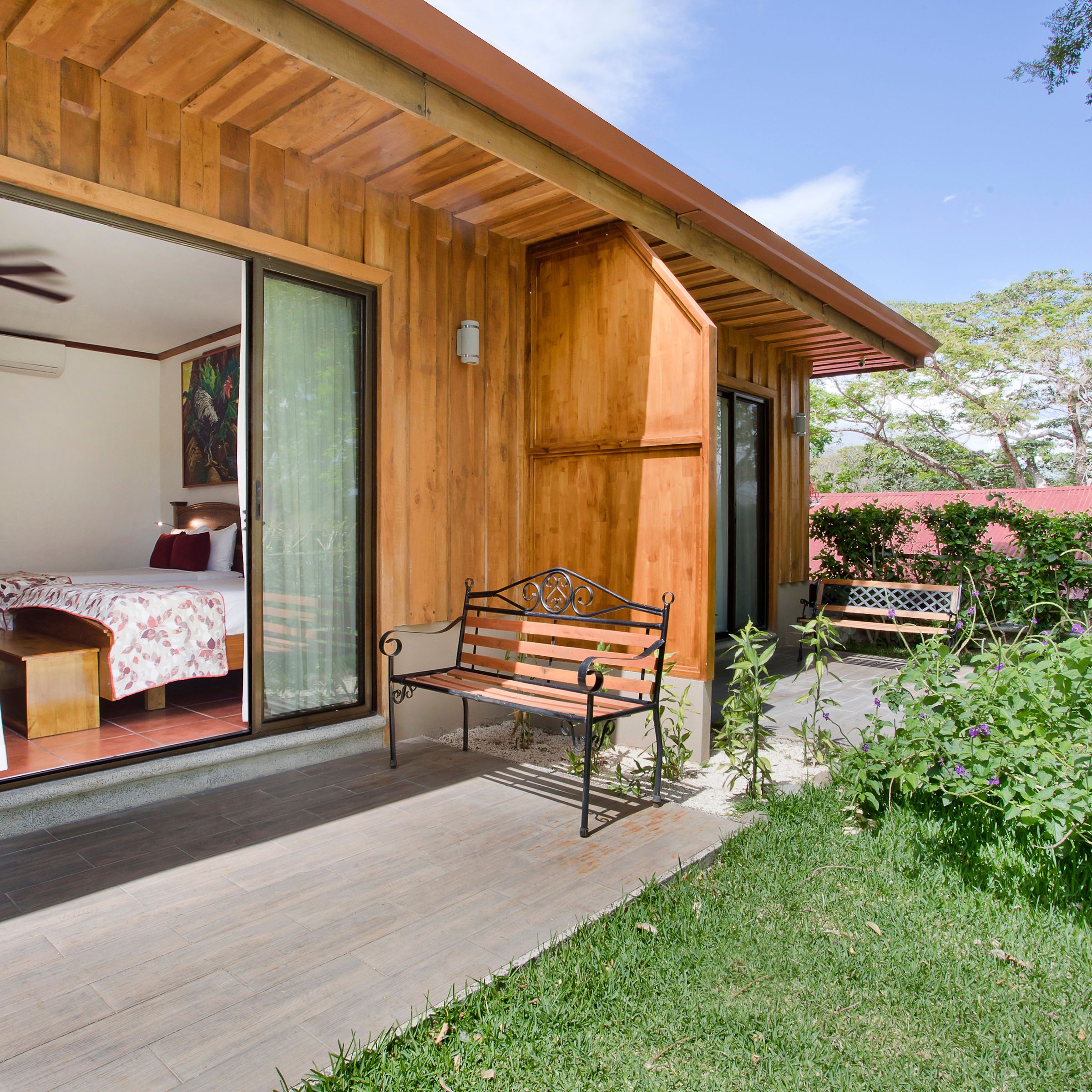 Wooden cabin with sliding doors opening to a room; outdoor bench on patio with garden view.