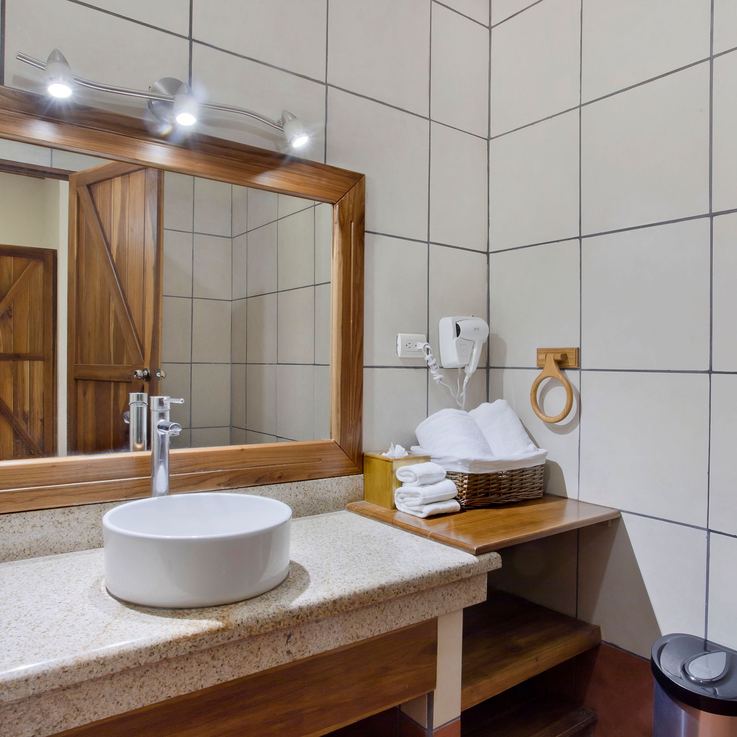 Modern bathroom with a round sink, large mirror, and wooden accents on countertop and shelves.