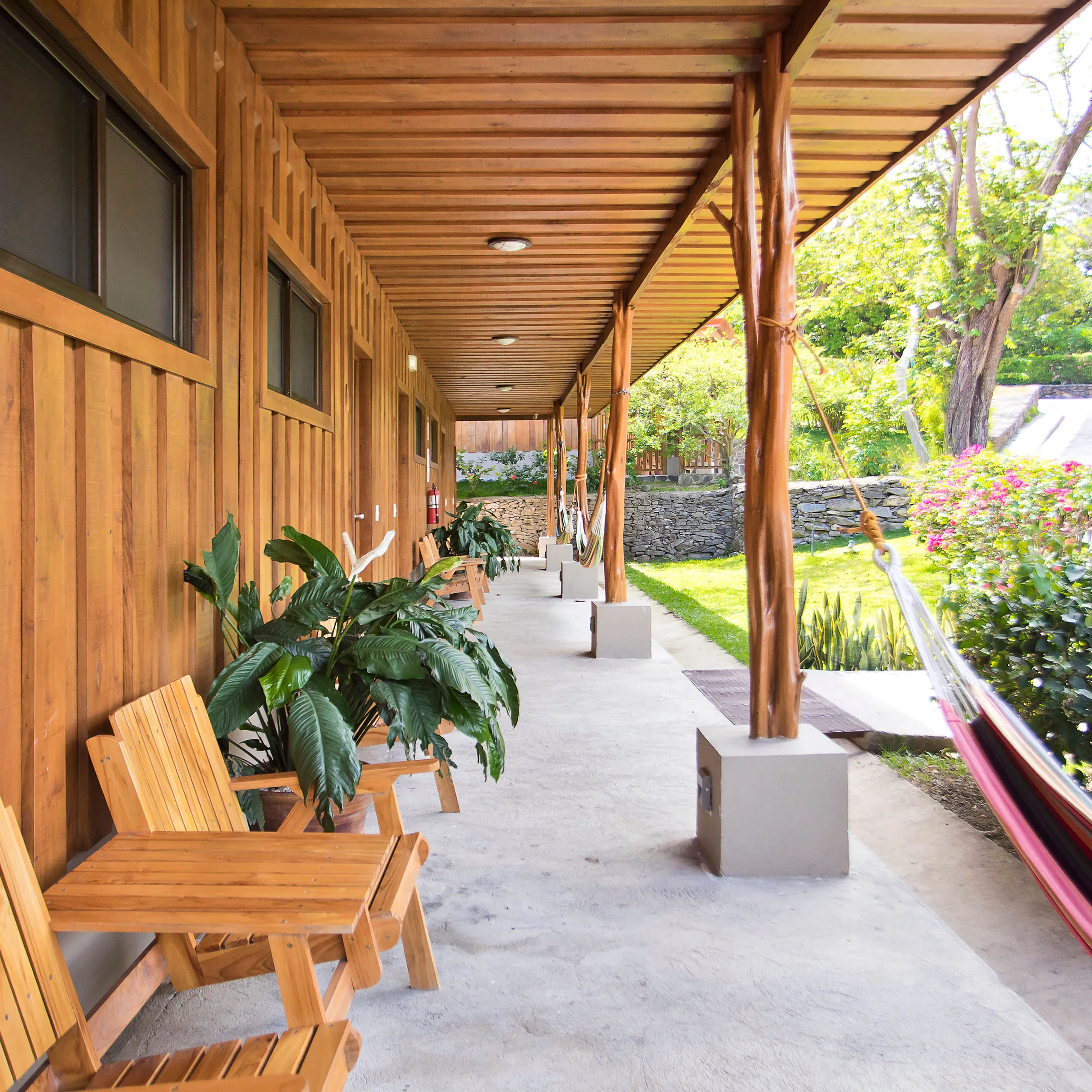 Wooden porch with chairs, plants, and hammocks overlooking a garden with stone path.