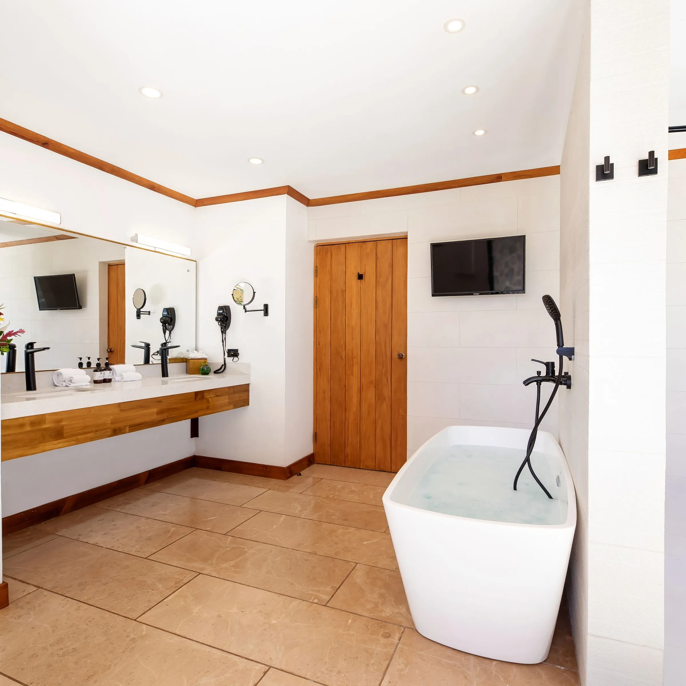 Modern bathroom with a freestanding tub, double sink vanity, and wall-mounted TV.