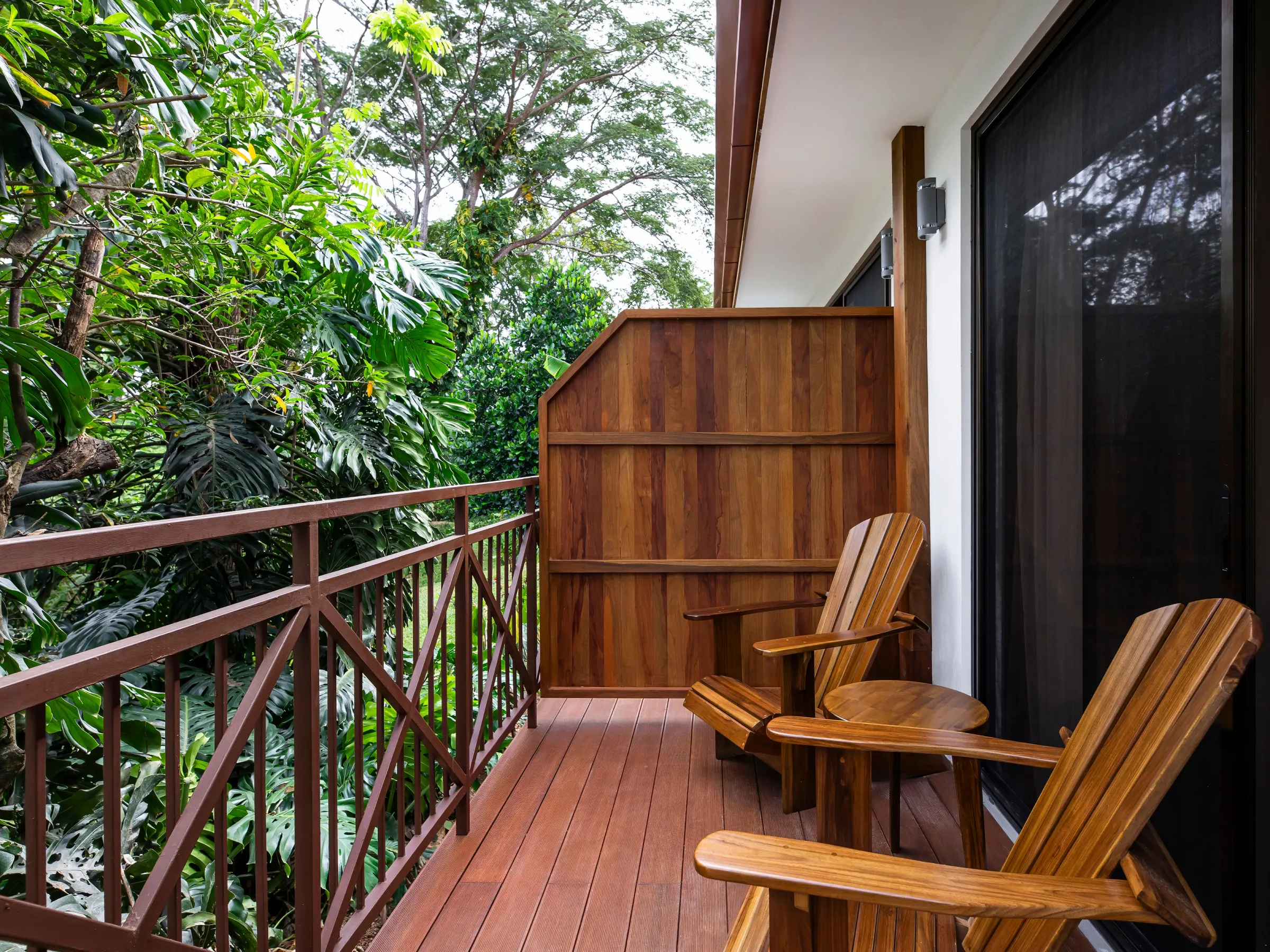 Wooden balcony with two chairs, surrounded by lush greenery.