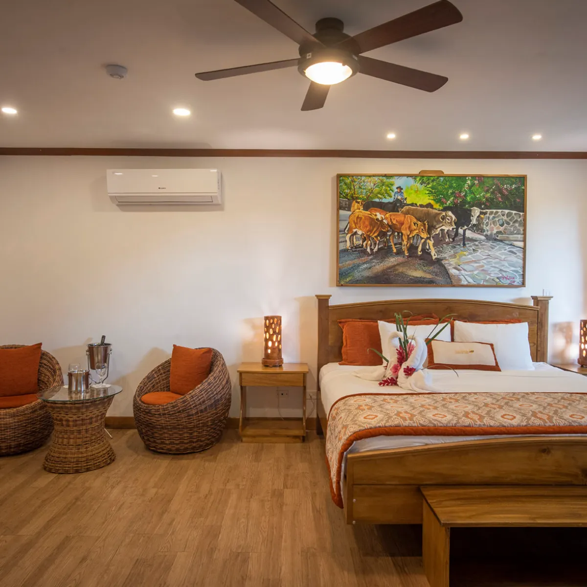 Cozy hotel room with wooden furniture, wicker chairs, floral bed, painting, and sliding door with garden view.