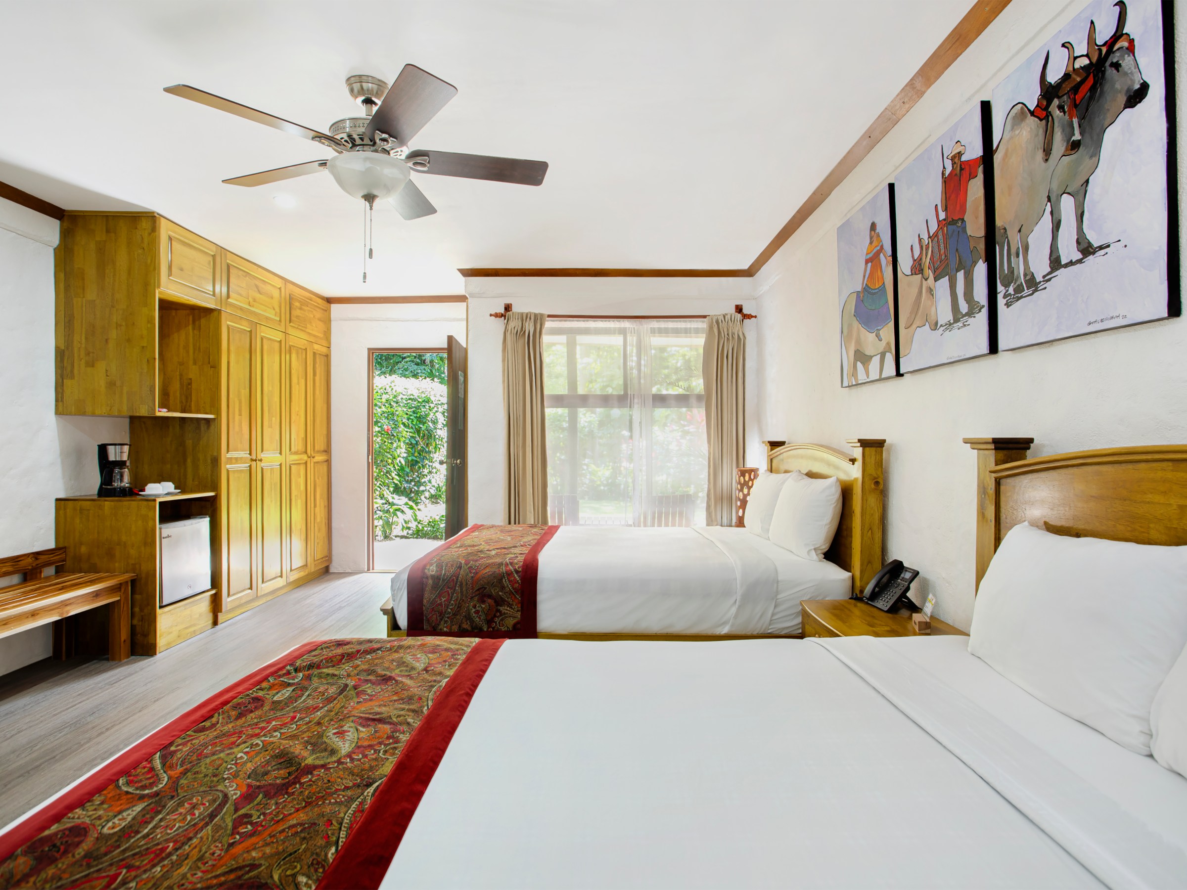 Bright hotel room with two beds, wooden furniture, and a large window with curtains.