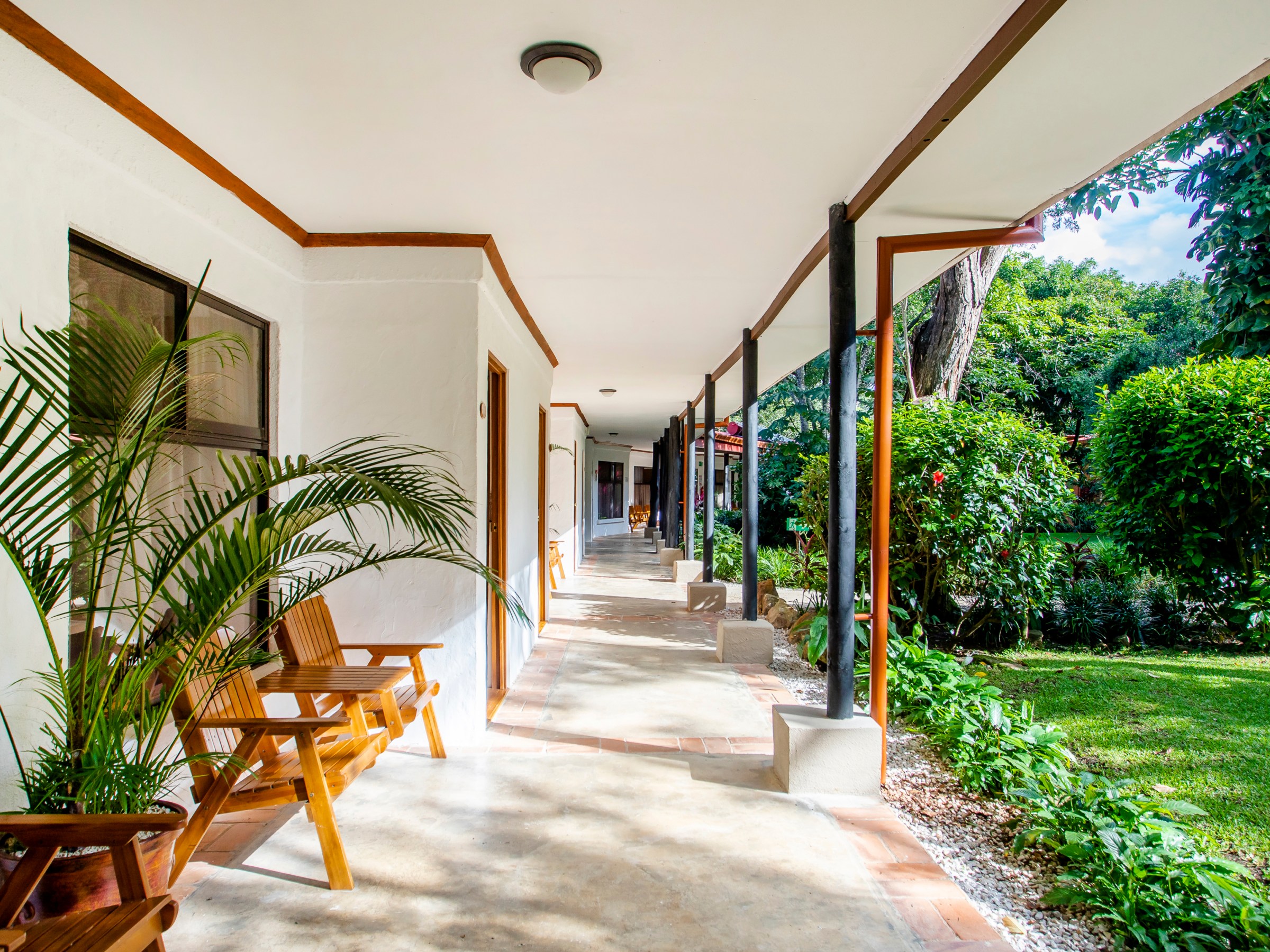 Covered outdoor corridor with wooden chairs and garden view.