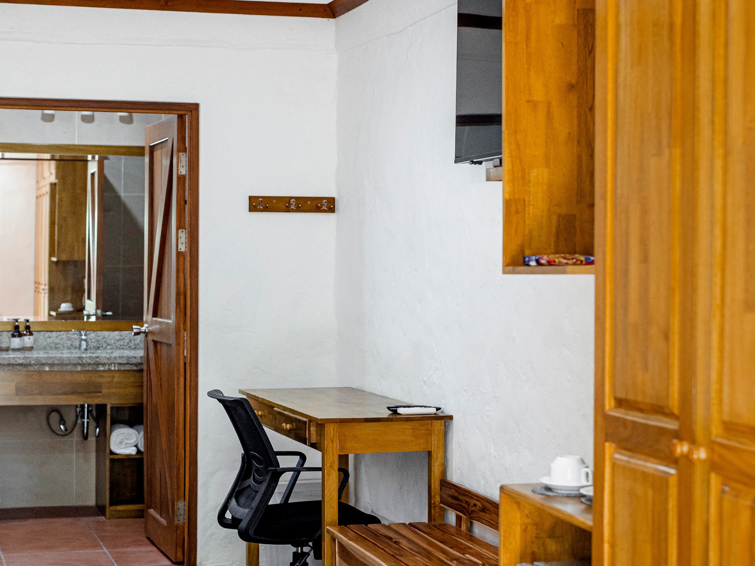 Room with wooden furniture, desk, chair, open door to bathroom, and wall-mounted TV.