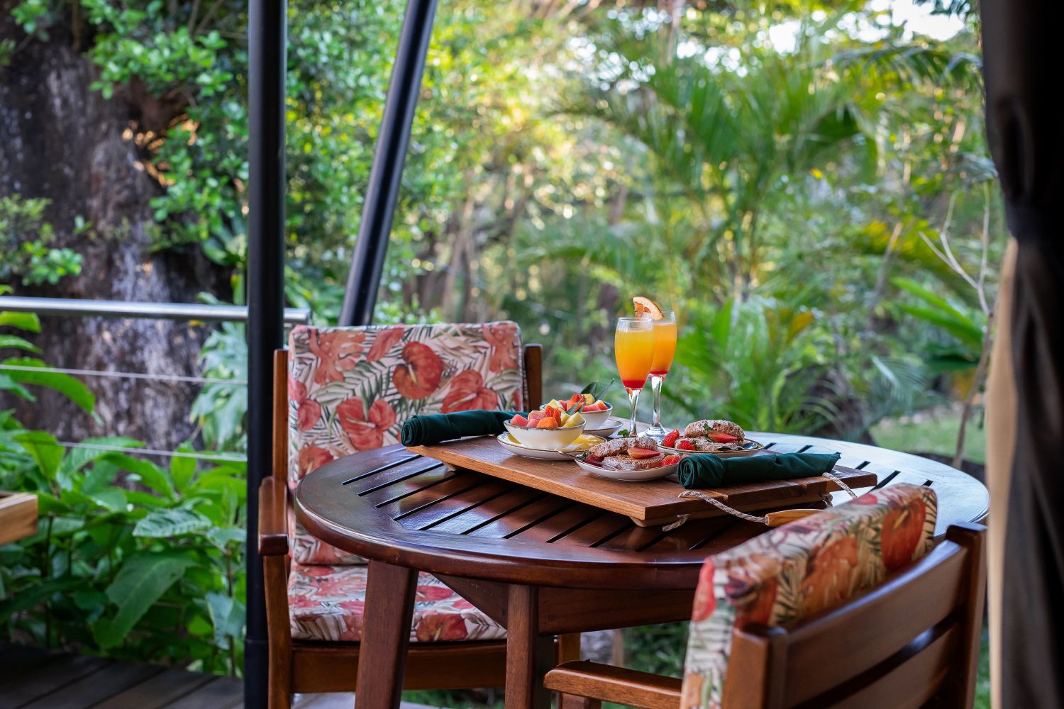 Tropical outdoor dining table with drinks and snacks on a wooden deck.