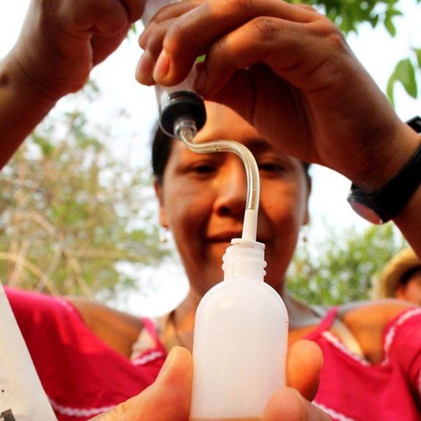 Person filling small bottle with liquid using a dropper.