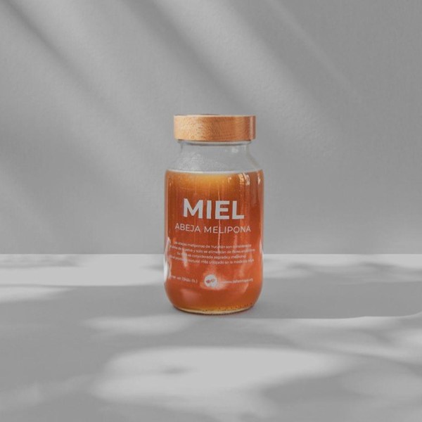 Jar of honey labeled 'Miel Abeja Melipona' with wooden lid on gray surface.