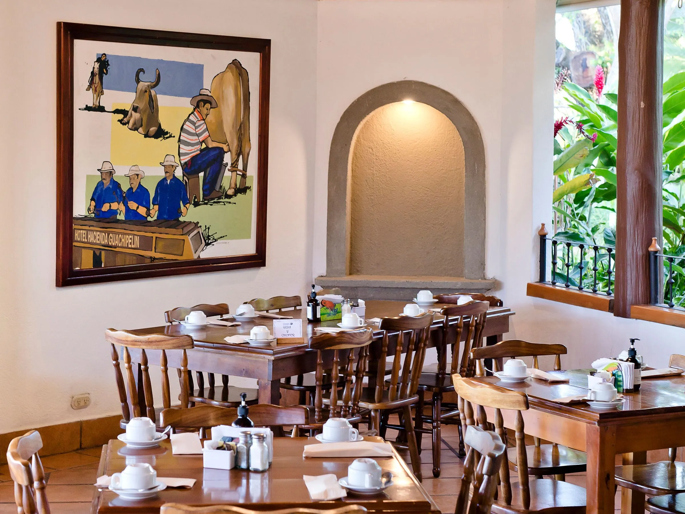 Cozy restaurant interior with wooden tables, chairs, and wall painting.