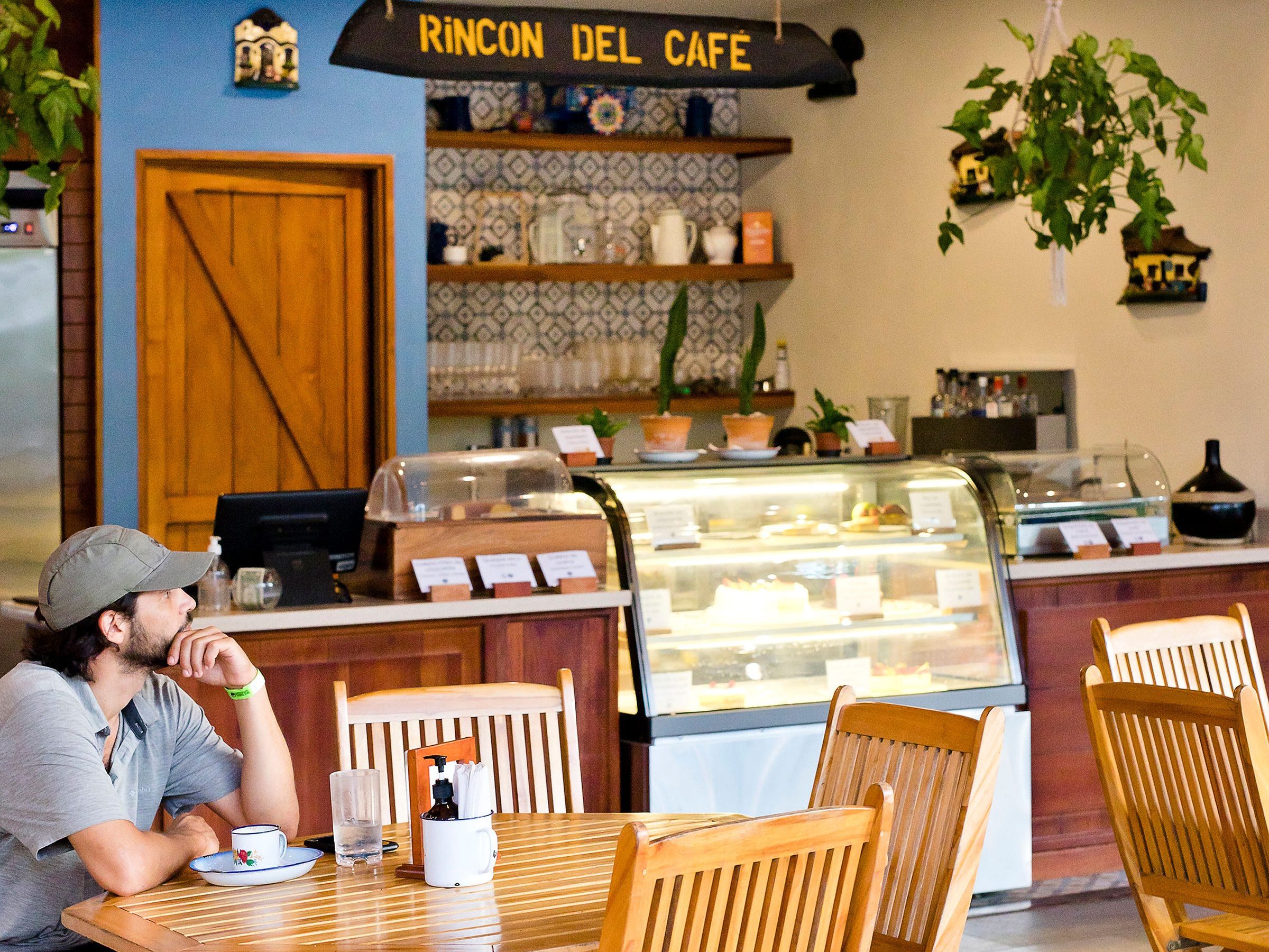 Man sitting at a wooden table in a cozy café with a lit dessert display.