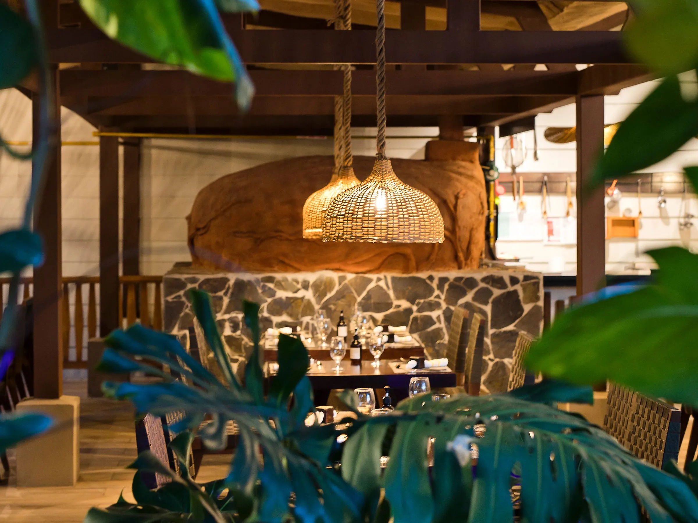 Cozy outdoor cafe with wood decor and hanging lamp, framed by lush green leaves.