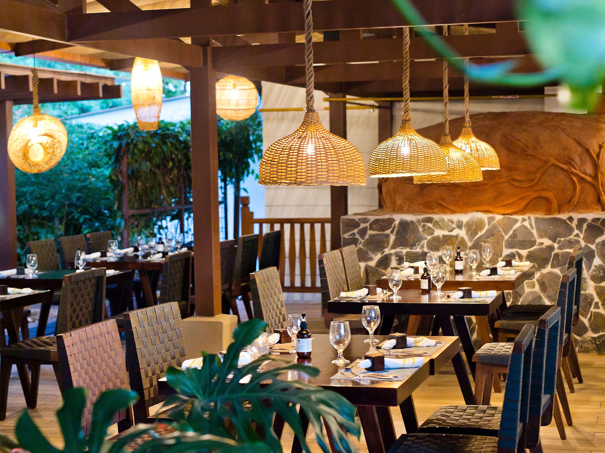 Cozy restaurant with wooden decor, plants, and wicker lamps.