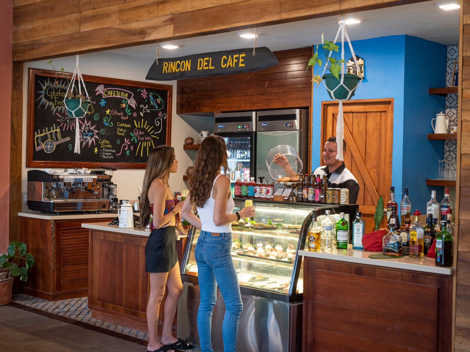 Two women at a café counter with pastries and beverages.