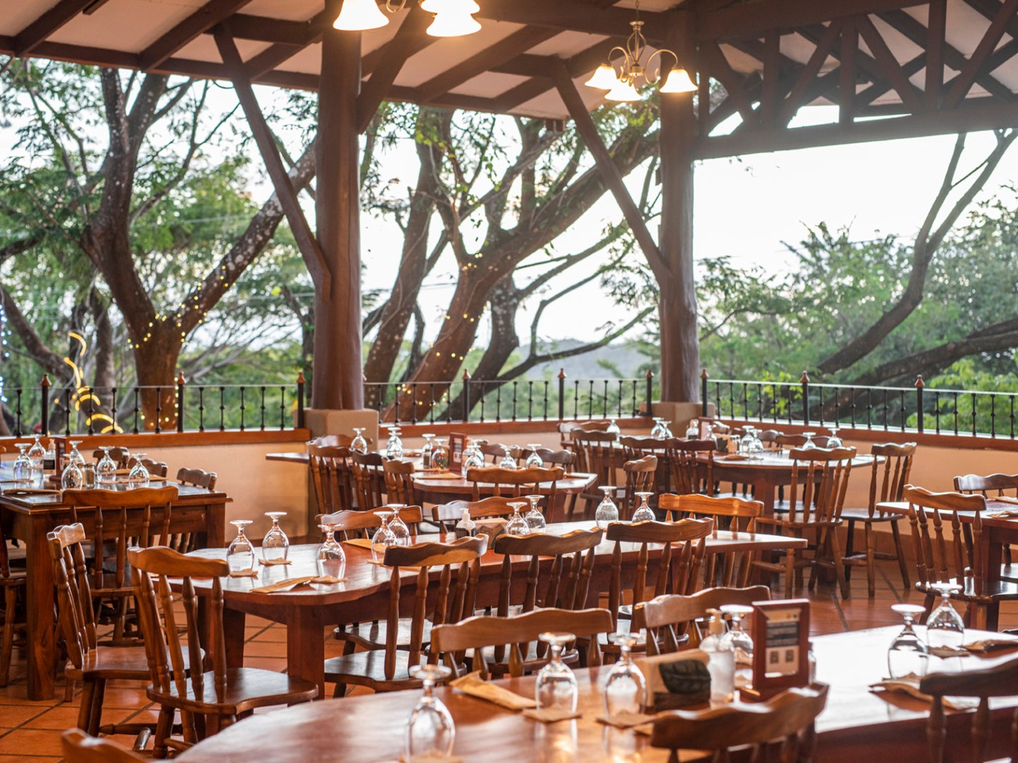 Outdoor restaurant with wooden tables and chairs, surrounded by trees.