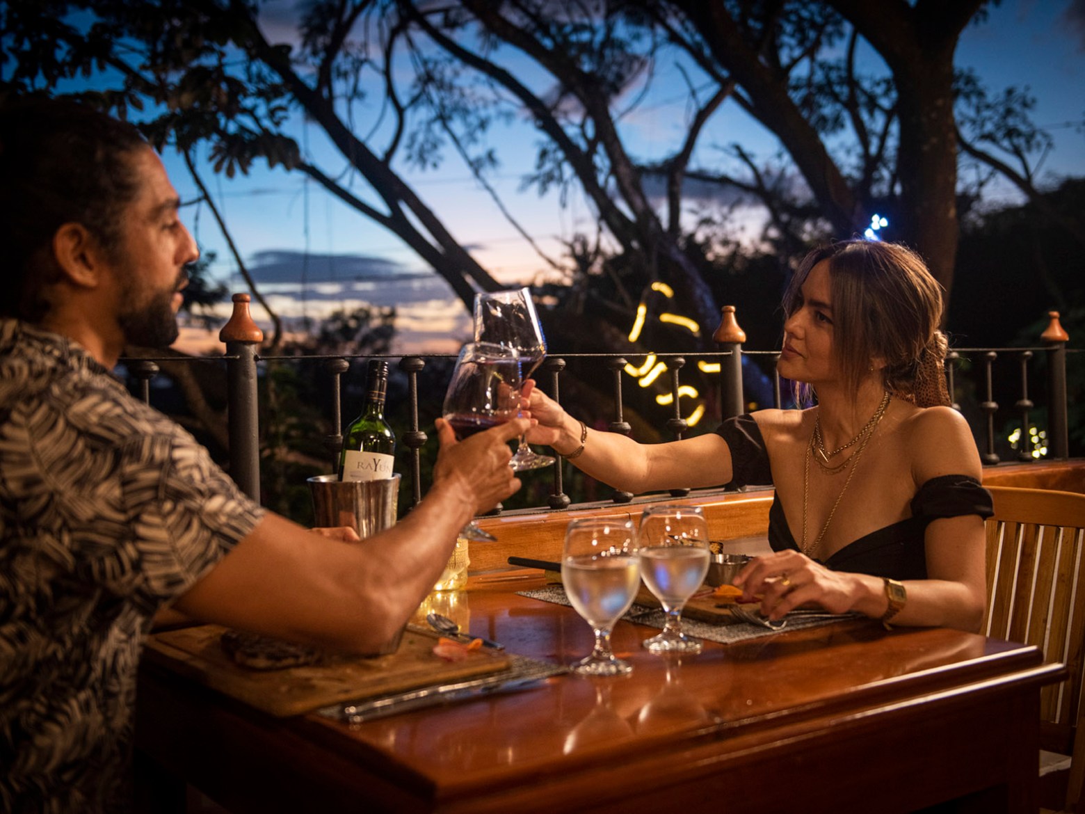 Couple clinking wine glasses at a sunset dinner outdoors.