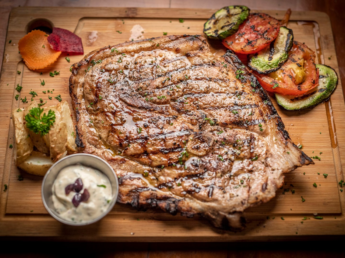 Grilled steak with vegetables and sauce on a wooden board.