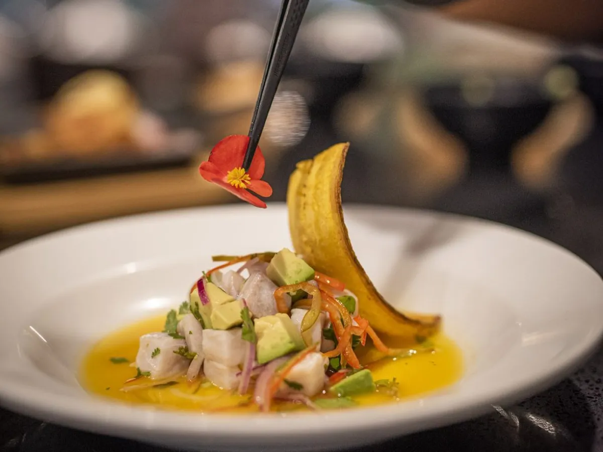 Chef garnishing ceviche dish with tweezers in a white bowl.