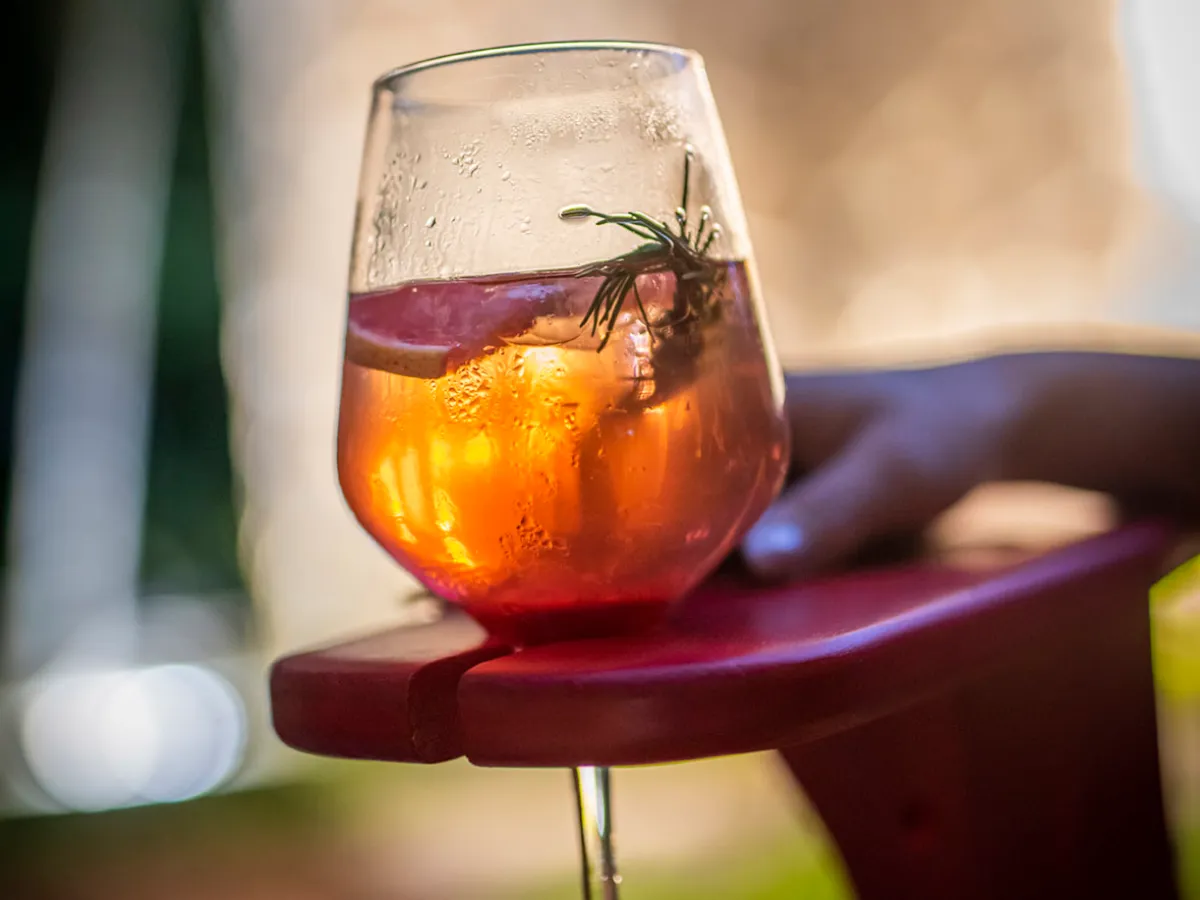 Glass of orange cocktail with rosemary on a red chair armrest.