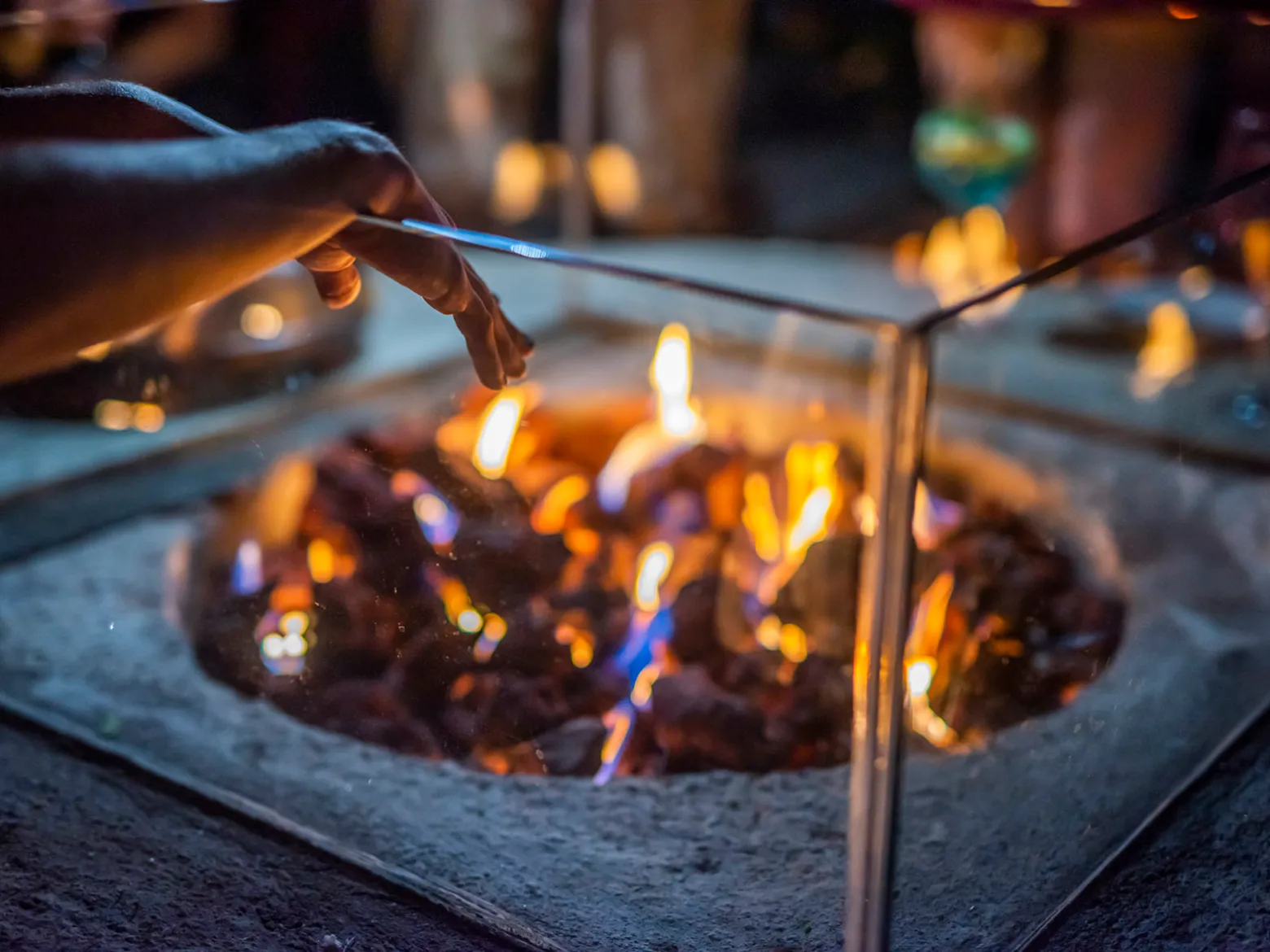 Hand warming over a glass-enclosed fire pit with visible flames.