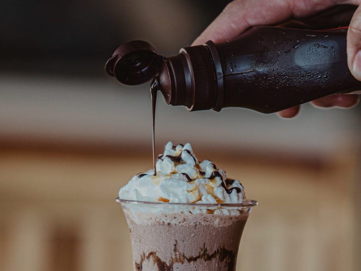 Chocolate drink with whipped cream being topped with syrup.