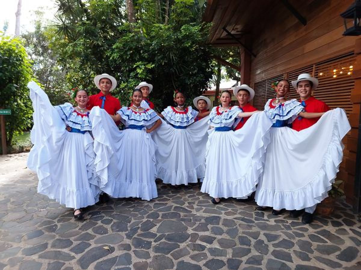 Group in traditional attire performing a folk dance on a stone path.