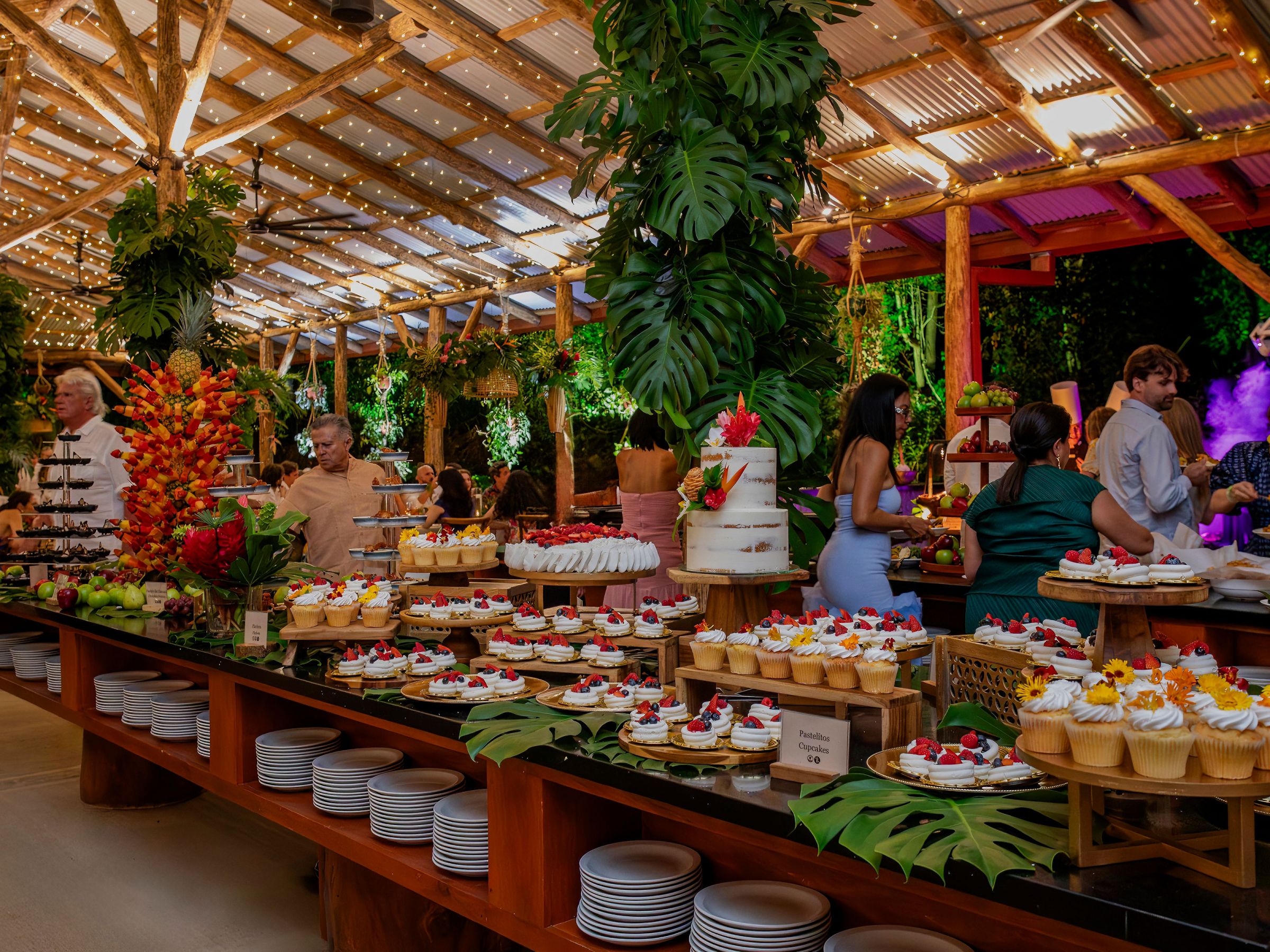 People at a lively indoor party with a variety of desserts on a large table.