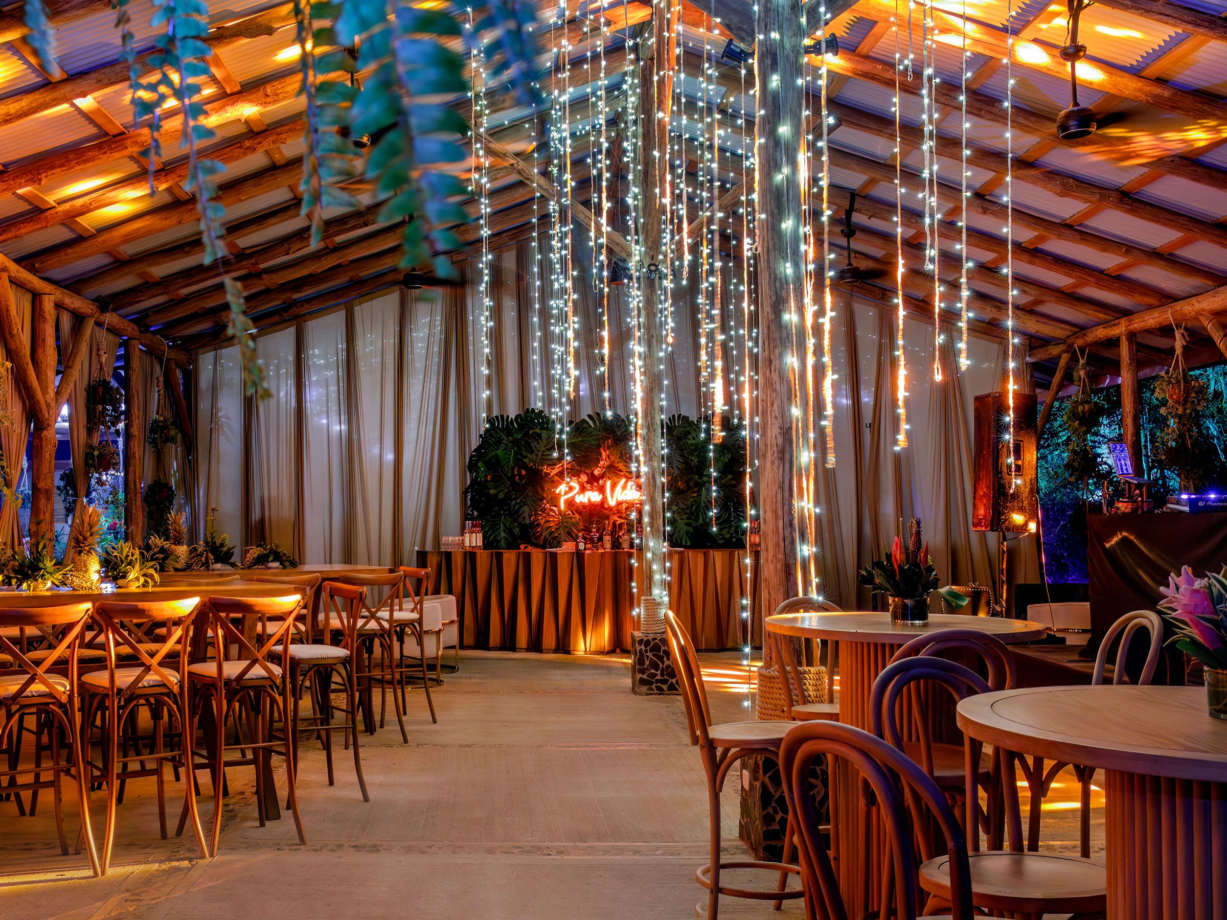 Warmly lit modern venue with hanging lights, tables, and chairs.