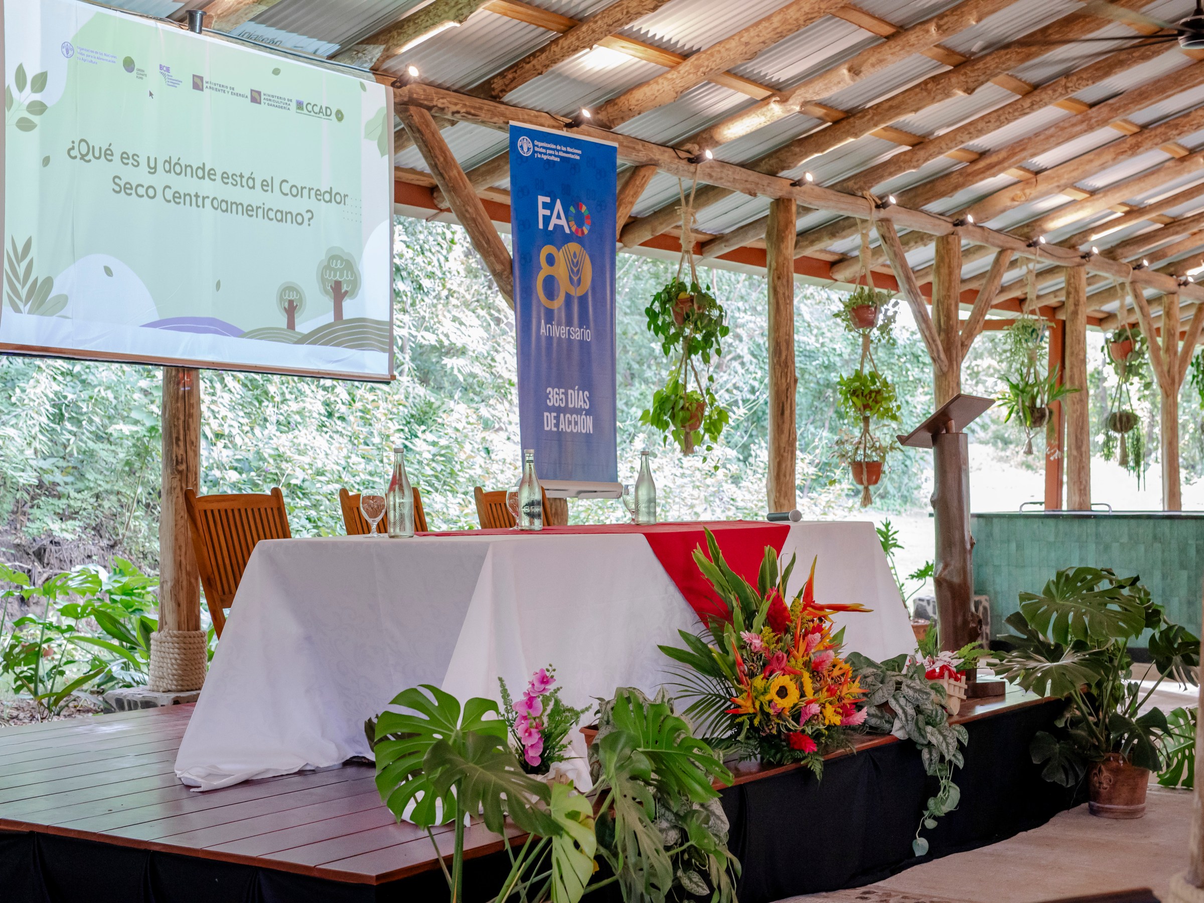 Outdoor stage with a presentation screen and decorated table with flowers.