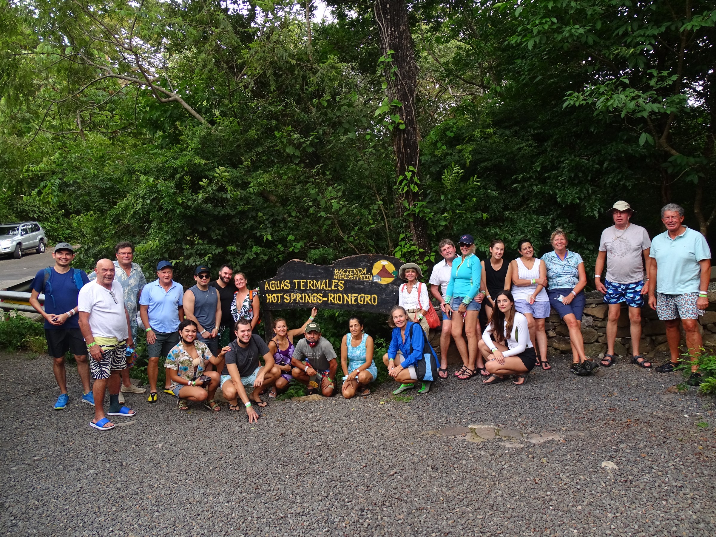 Group of people posing in front of a sign in a forested area.