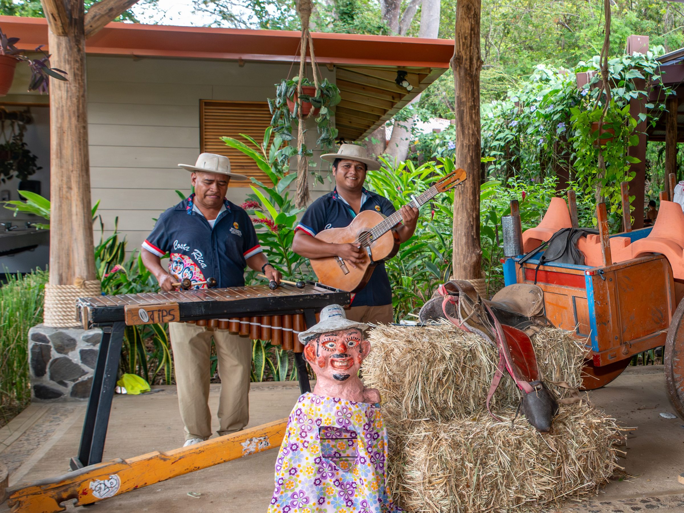 Musicians and couple in straw hat setting with hay bales and cart.