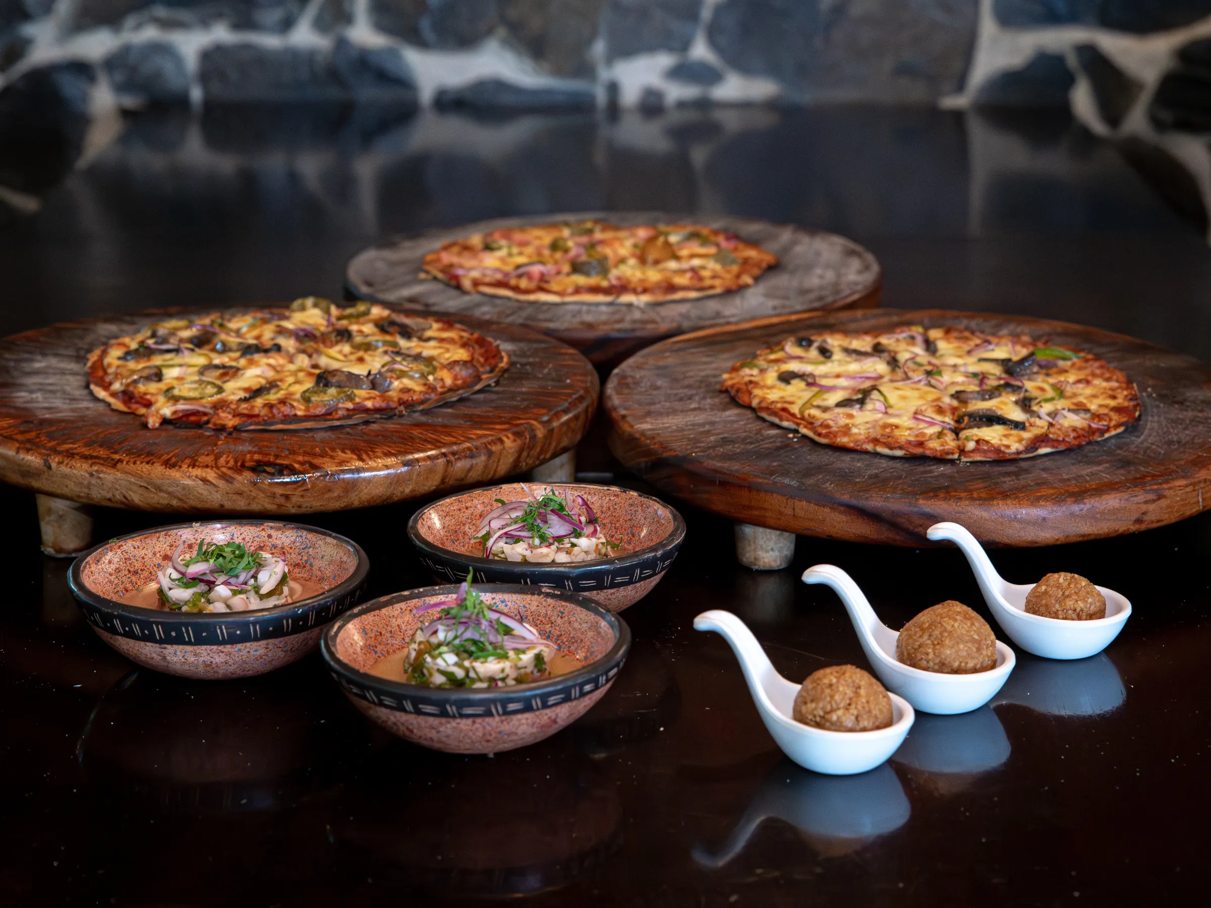 Three pizzas on boards with small bowls and spoons of appetizers.