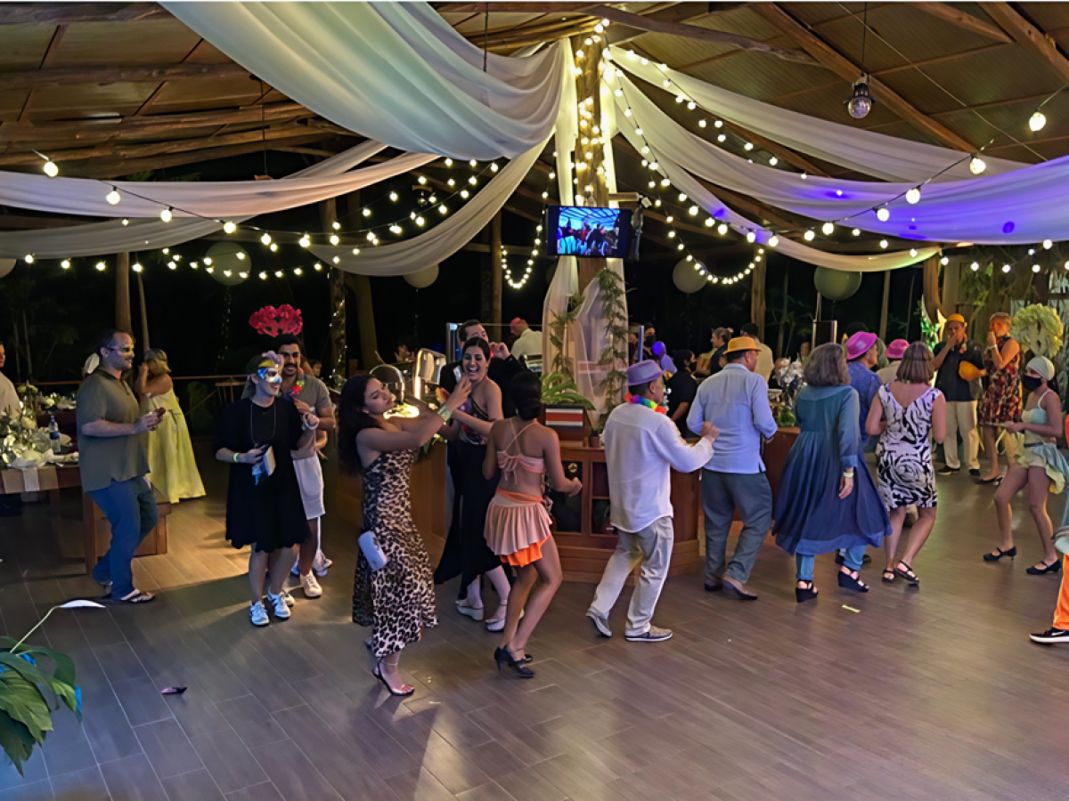 People dancing at a festive event with string lights and draped fabric decorations.