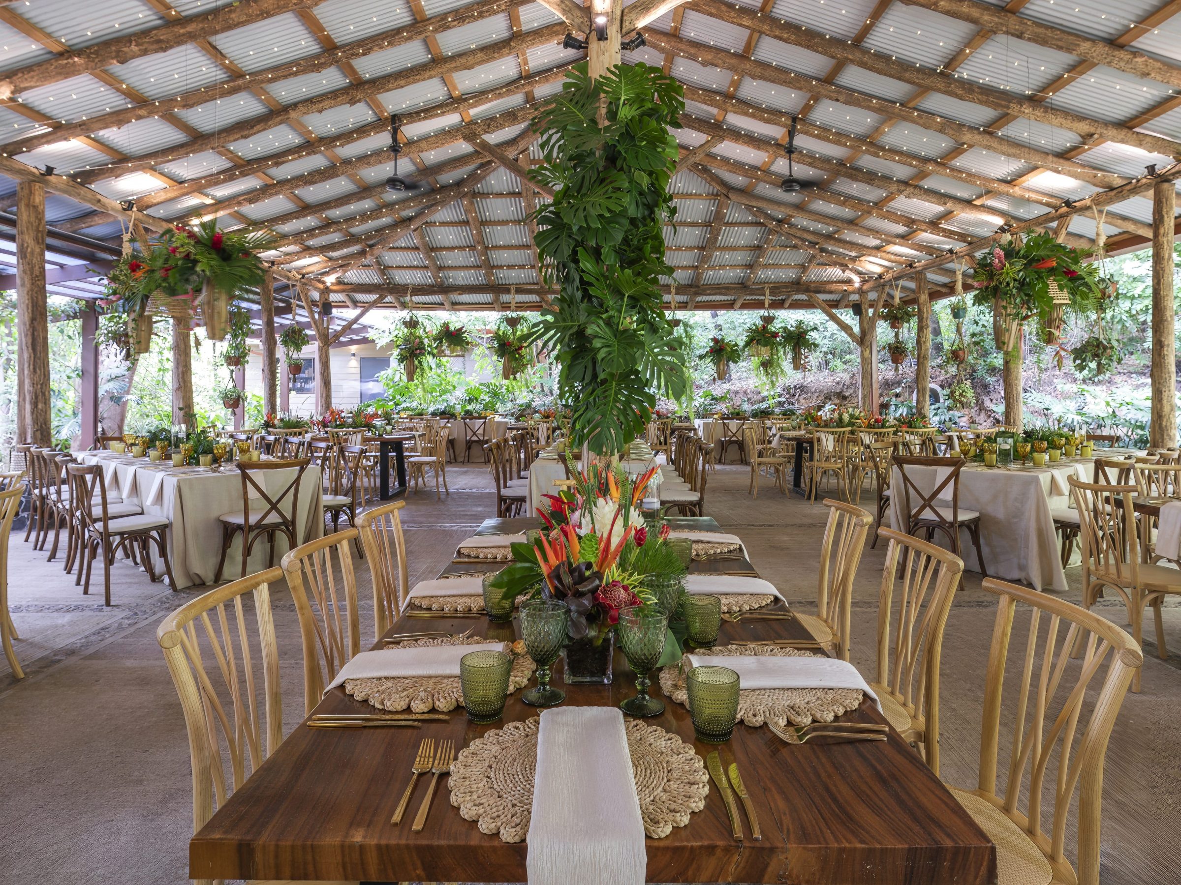 Rustic open-air dining area with wooden tables, chairs, and hanging plants.