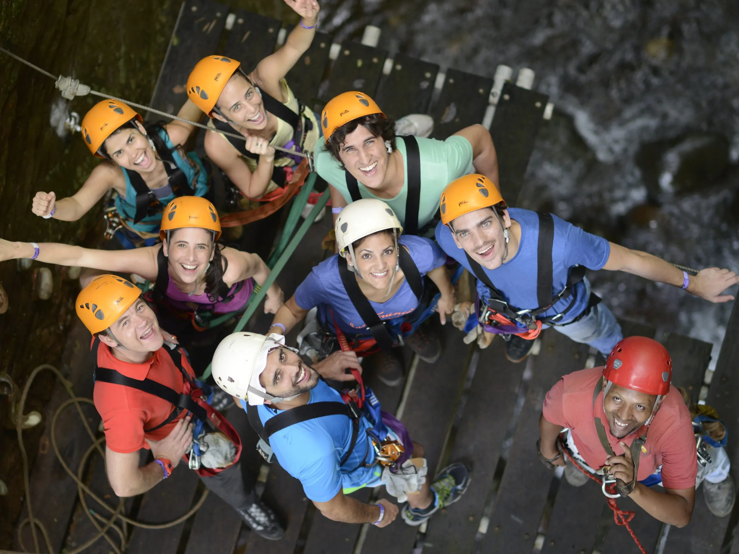 Group of people with helmets and harnesses on a wooden platform looking up.