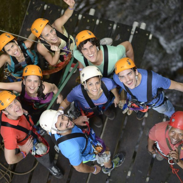 Group of people with helmets and harnesses on a wooden platform looking up.