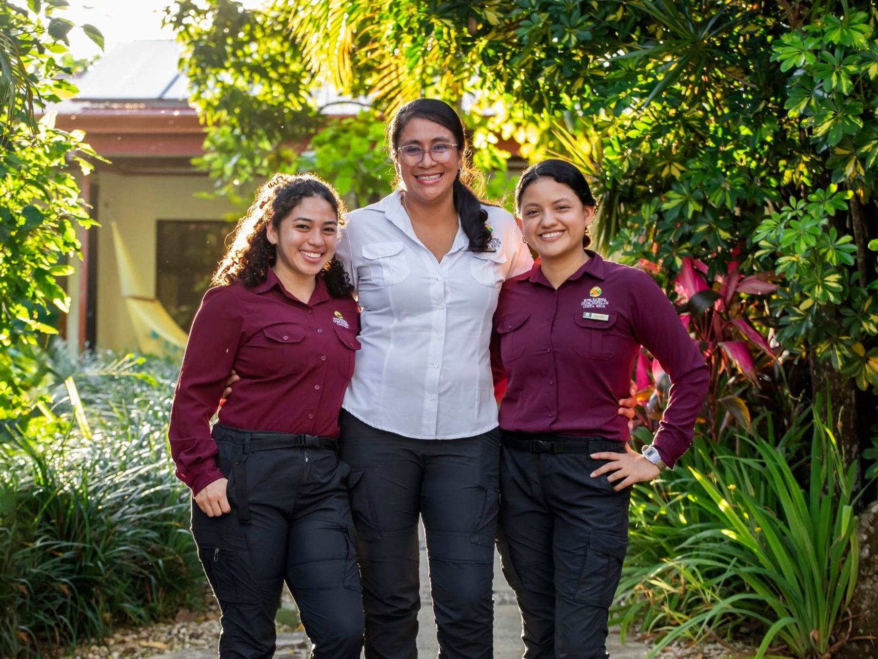 Three women in uniforms smiling and standing outside on a garden path.