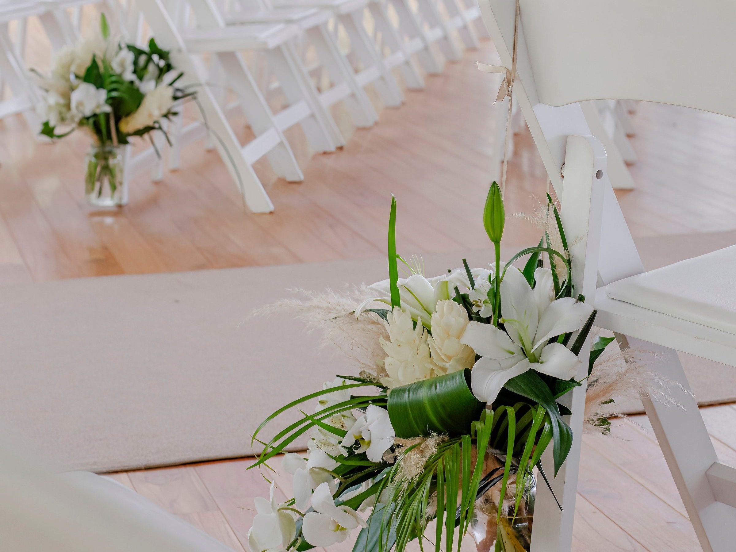 White chairs arranged in rows for a wedding, with floral decorations on a wooden floor.