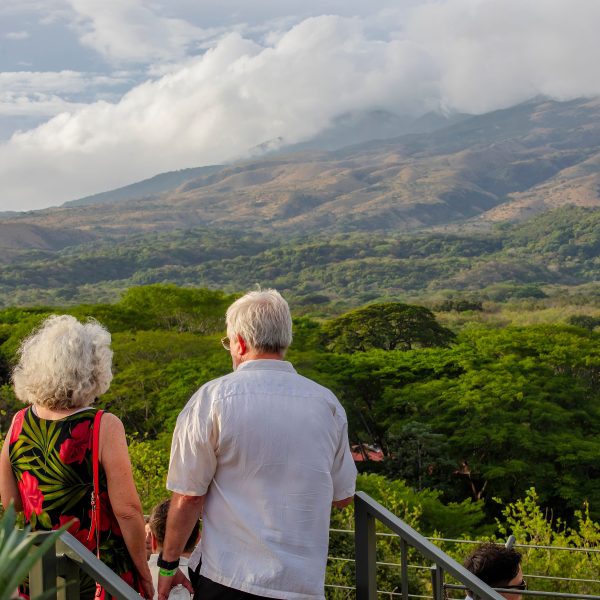Elderly couple on steps overlooking lush green landscape and mountains.