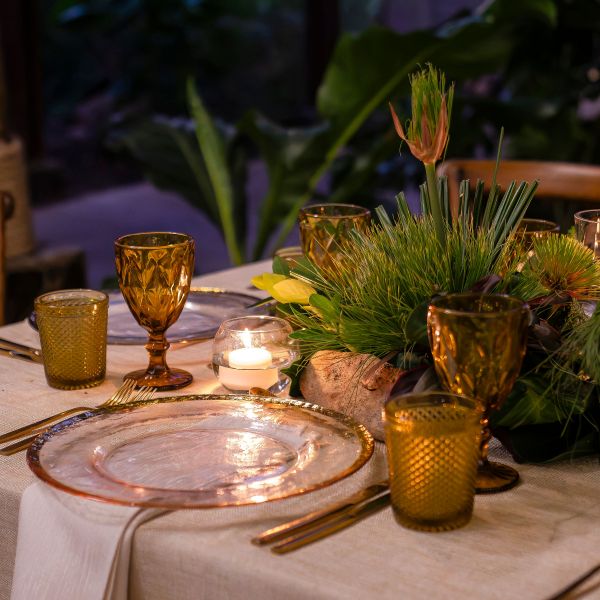 Elegant table setting with amber goblets, greenery, and candles.