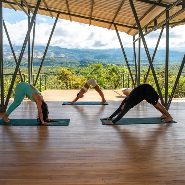 Three people practicing yoga in a pavilion with mountain view.