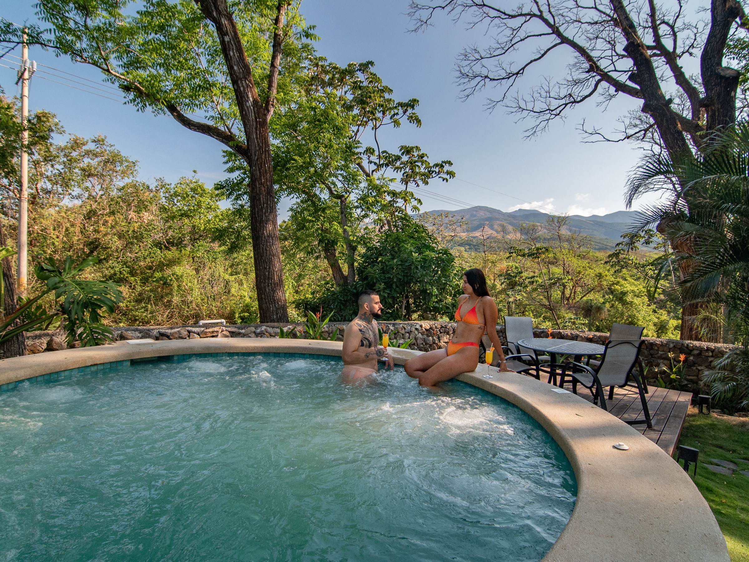Two people conversing in a round outdoor pool surrounded by trees.