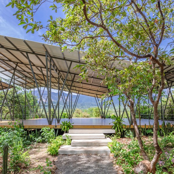 Modern pavilion with open sides in a lush garden setting, surrounded by trees.
